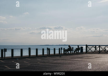 Milford on Sea, Großbritannien - 13 Juli 2019: Menschen sitzen auf Bänken, Lesen durch das Meer in Milford on Sea, einem traditionellen englischen Dorf, das bekannt ist für breathta Stockfoto