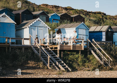 Milford on Sea, Großbritannien - 13 Juli, 2019: Junge Menschen, die sich durch die bunten Badekabinen in Milford on Sea, einem traditionellen englischen Dorf, das bekannt ist für Atem Stockfoto