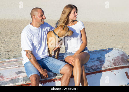 Junge Erwachsene Paar mit Hund einen entspannenden Spaziergang am Sandstrand Stockfoto