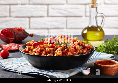 Nahaufnahme der Kichererbsen fritos, heiße Kichererbsen Eintopf mit Chorizo, Tomaten und Gewürzen in einem schwarzen Schüssel auf einen konkreten Tisch mit Inhaltsstoffen in der backgrou Stockfoto