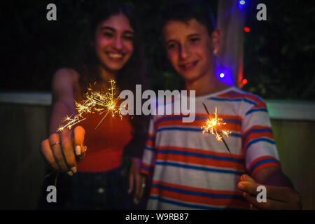 Junge Freunde, Party mit Feuerwerk im Freien auf der Terrasse. Lächelnde Mädchen und Jungen Spaß genießen Wunderkerzen bei Familie Geburtstag. Paar Bruder Stockfoto