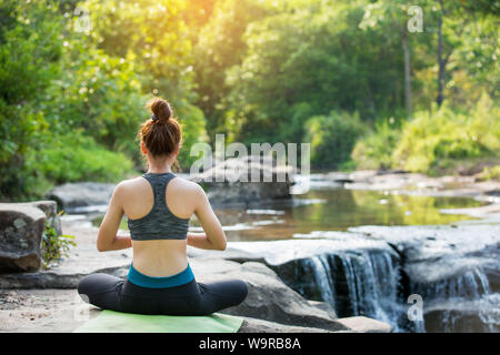 Asiatische junge Frau Yoga in der Nähe von Wasserfall Stockfoto