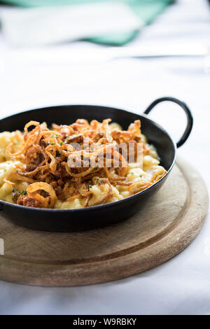 In der Nähe der traditionellen alpinen Kässpatzen in eine eiserne Pfanne auf einem Holzbrett serviert. Stockfoto