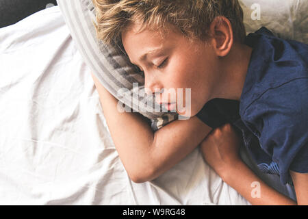 Junge Schlafen mit den Händen auf das Kissen. Schönes Kind schläft alleine im Bett träumen von Urlaub. Jugendlich ist Ruhe zu Hause angenehm entspannen Stockfoto