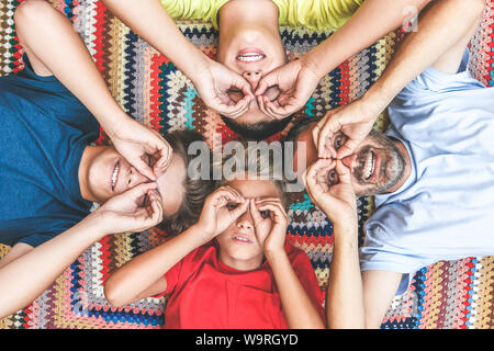 Vater und Söhne gemeinsam genießen, liegend auf einer bunten Decke. Vier Männer unterschiedlichen Alters machen das Teleskop mit ihren Händen. Dabei auf eine Gruppe von Menschen Stockfoto