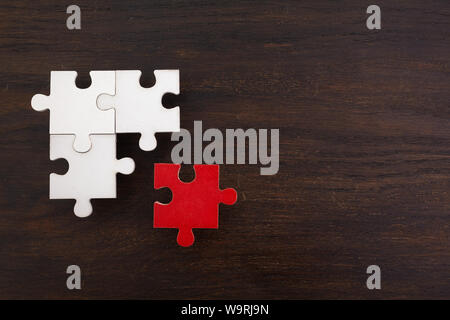 Drei onnected Puzzle Stücke und ein Rot auf Schwarz Holz- Hintergrund. Das Konzept der Suche nach richtigen Lösungen in Teamarbeit. Stockfoto