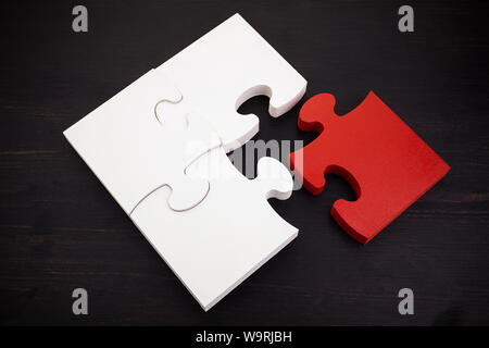 Drei onnected Puzzle Stücke und ein Rot auf Schwarz Holz- Hintergrund. Das Konzept der Suche nach richtigen Lösungen in Teamarbeit. Stockfoto