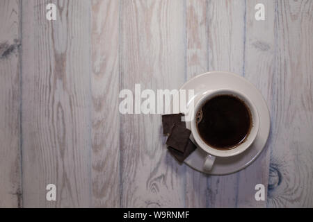 Schwarzer Kaffee in weisser Tasse mit Untertasse und Stücke Schokolade auf dem Tisch obere Ansicht, Hintergrund für Text Stockfoto