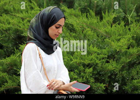 Junge muslimische Frau mit Smartphone im Alexandergarten. Hübsches Mädchen im Hijab in einem Sommer Park Stockfoto