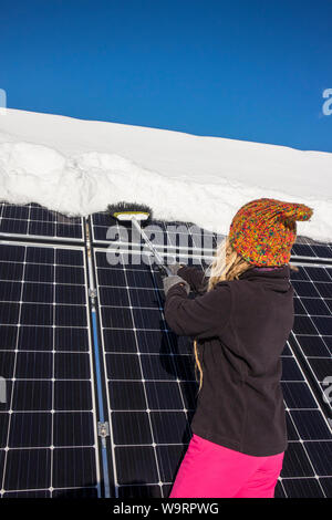 Frau schieben Schnee Solarmodule aus im Winter. Wenn Schnee Panels umfasst, können Sie nicht Strom erzeugen. Die kleinen privaten Home Haus im Hintergrund. Stockfoto