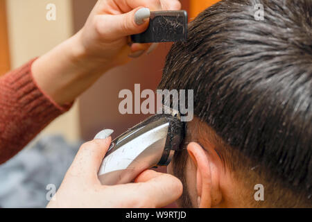 Frau Friseur schneidet die Haare des Mannes mit elektrischer Haarschneider Trimmer Stockfoto