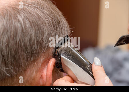 Frau Friseur schneidet die Haare des Mannes mit elektrischer Haarschneider Trimmer Stockfoto