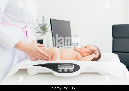 Süße kleine Baby liegend auf Waagen, medizinische Überprüfung, in der Klinik, zu kopieren. Junge weibliche Kinderarzt Arzt untersucht, Baby. Stockfoto