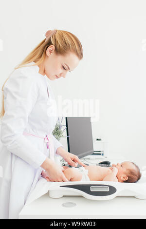 Süße kleine Baby liegend auf Waagen, medizinische Überprüfung, in der Klinik, zu kopieren. Junge weibliche blond Kinderarzt Arzt untersucht, Baby. Stockfoto