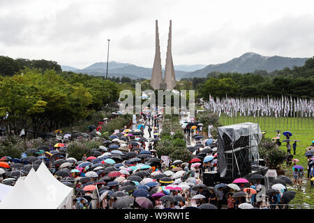 Cheonan, Südkorea. 15 Aug, 2019. 15.August 2019 - Cheonan, South Korea-People holding Sonnenschirme sehen Sie hier einen TV-Bildschirm während der Veranstaltung für den 74. Jahrestag der Unabhängigkeit Koreas Tag an der Halle der Unabhängigkeit Koreas in Cheonan, Südkorea, am Donnerstag, 15 August, 2019. Quelle: Bloomberg über Pool/ZUMA Draht/Alamy leben Nachrichten Stockfoto
