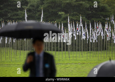 Cheonan, Südkorea. 15 Aug, 2019. 15.August 2019 - Cheonan, Südkorea - ein Mann mit einem Regenschirm Spaziergänge letzten nationalen Südkoreas Fahnen auf der Independence Hall von Korea in Cheonan, Südkorea, am Donnerstag, 15 August, 2019. Quelle: Bloomberg über Pool/ZUMA Draht/Alamy leben Nachrichten Stockfoto