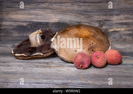 Frische Portobello Pilze und Lychee Früchte close-up auf einer hölzernen Oberfläche Stockfoto