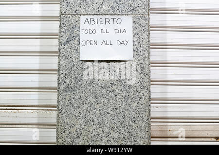 Ein Zeichen in Spanisch und Englisch sprach den ganzen Tag geöffnet außerhalb einer geschlossenen Shop in Spanien. Stockfoto