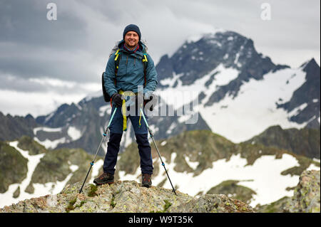 Wanderer Mann steht auf der Klippe gegen den Gipfel eines Berges. Der Mensch hat einen Rucksack und Wanderstöcke. Mountain Trekking. Platz kopieren Stockfoto