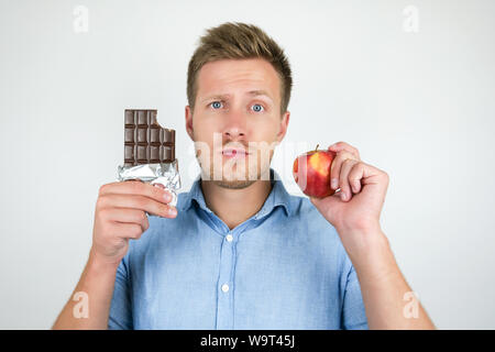 Jungen gutaussehenden Mann mit Schokolade in der einen Hand und Frische reifer Apfel in einem anderen zeigen Kontrast auf isolierten weißen Hintergrund. Stockfoto