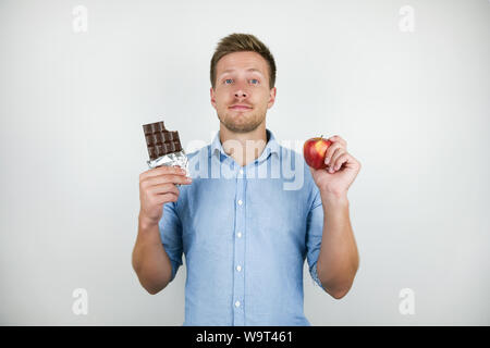 Jungen gutaussehenden Mann mit Schokolade in der einen Hand und Frische reifer Apfel in einem anderen auf isolierten weißen Hintergrund. Stockfoto