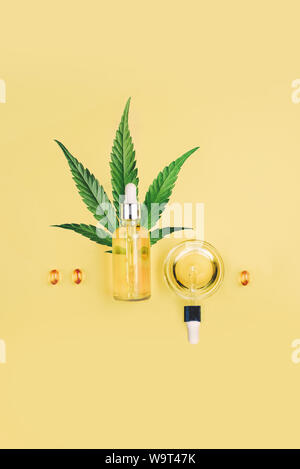 Flasche mit CBD Öl, Pipette, Kapseln und Cannabis Blatt auf einem gelben Hintergrund. Minimalismus, flach. Stockfoto