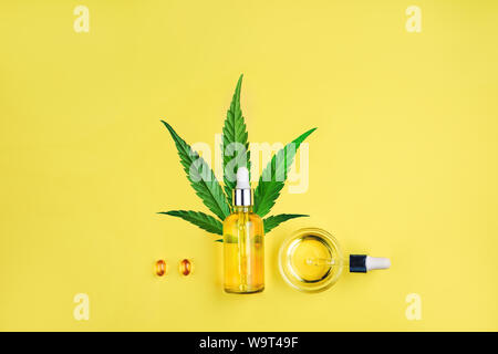 Flasche mit CBD Öl, Pipette, Kapseln und Cannabis Blatt auf einem gelben Hintergrund. Minimalismus, flach. Stockfoto