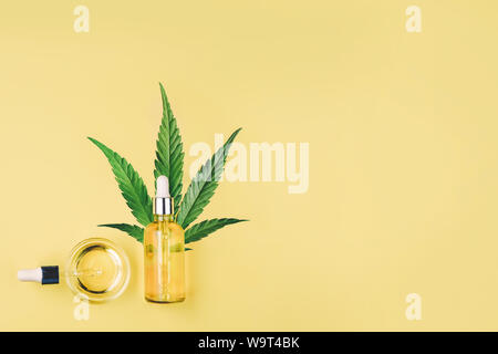 Flasche mit CBD Öl, Pipette, Kapseln und Cannabis, Hanf Blatt auf einem gelben Hintergrund. Minimale Zusammensetzung, flach. Stockfoto