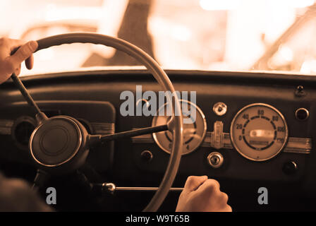 Fahren Oldtimer; nur die Hand des Fahrers auf das Lenkrad sind sichtbar, das Armaturenbrett ist verschwommen; stilisierte als Alter sepia Foto mit Staub eine Stockfoto