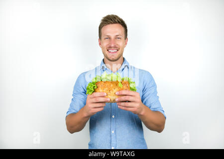 Jungen gutaussehenden Mann sieht hungrig, hungrig und glücklich halten frische Sandwich mit Salat auf isolierten weißen Hintergrund. Stockfoto