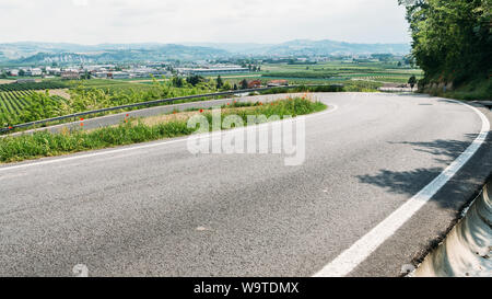 Malerischer Blick auf eine geschwungene Straße unter Weinberg Hügel und das Tal gegen einen bewölkten Himmel im Frühling, Barbaresco, Langhe, Piemont, Italien. Stockfoto