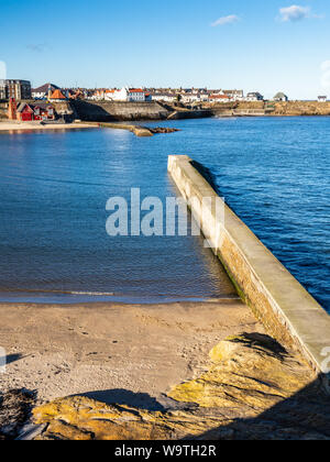 Die Sonne scheint auf der Hafenmauer Wellenbrechern und Rettungsboot station am Cullercoats Bucht in Tyneside. Stockfoto