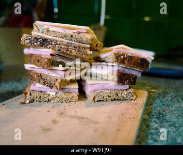 Sandwich mit Käse und Schinken auf Schneidebrett in der verschwommenen Küche Hintergrund. Close Up. Stockfoto