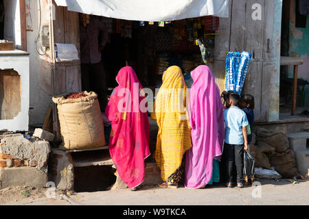 Drei Frauen in bunten Saris vor einem Geschäft holzbilderrahmen (Rücken zur Kamera), zwei Kinder stehen neben ihnen. Straßenszene in Mandawa (Rajasthan) in Ind Stockfoto