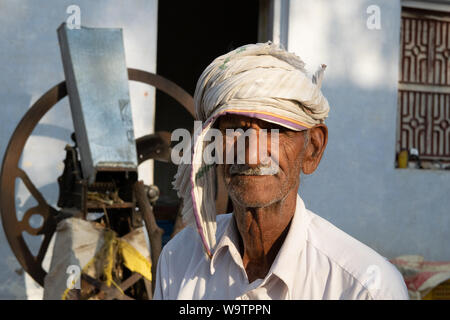 Ein alter Mann sitzt in einem Hof vor seinem Haus. Auf dem Kopf trägt er ein Tuch (Turban). Straßenszene in Mandawa (Rajasthan) Stockfoto