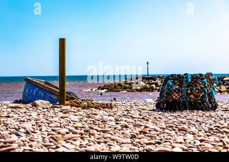 Ein altes Fischerboot und Netze verlassen auf einem Kiesstrand in Sidmouth. Stockfoto