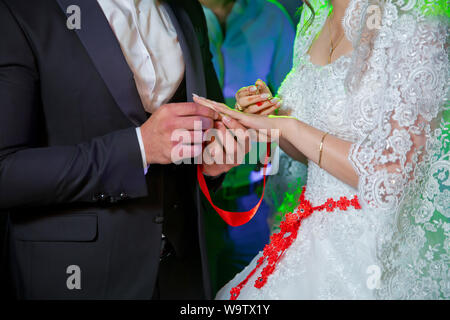 Setzt einen Ring an die Hand der Braut. Bräutigam Hochzeit Ring setzt auf's Braut Hand in Kirche. Mann legt einen Ehering an Hand einer Braut, Nahaufnahme Stockfoto