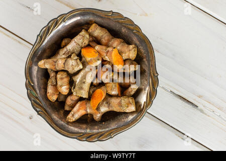 Menge Menge Scheiben von hellen Gelbwurz Rhizom in Altes Eisen Schüssel flatlay auf weißem Holz Stockfoto