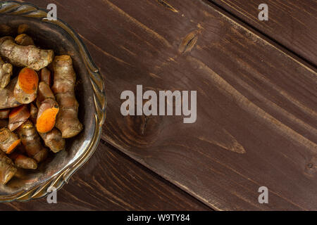 Menge Menge Scheiben von hellen Gelbwurz Rhizom copyspace Rechts in Altes Eisen Schüssel flatlay auf braunem Holz Stockfoto