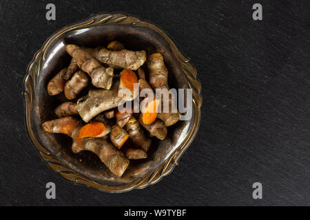 Menge Menge Scheiben von hellen Gelbwurz Rhizom in Altes Eisen Schüssel flatlay am grauen Stein Stockfoto