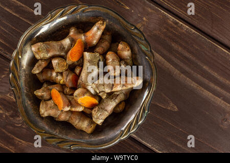 Menge Menge Scheiben von hellen Gelbwurz Rhizom in Altes Eisen Schüssel flatlay auf braunem Holz Stockfoto