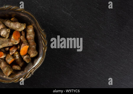 Menge Menge Scheiben von hellen Gelbwurz Rhizom copyspace Rechts in Altes Eisen Schüssel flatlay am grauen Stein Stockfoto