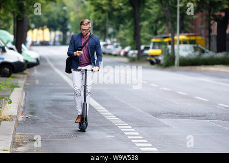 Ein junger Geschäftsmann mit Mobiltelefon, einen Elektroroller auf der Straße Stockfoto
