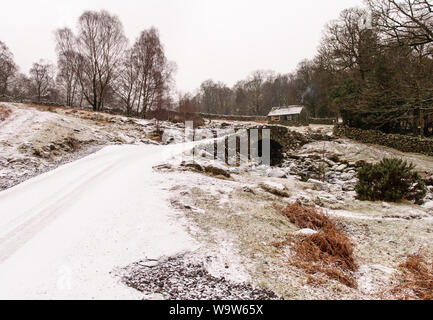 Winterschnee liegt auf der malerischen Steinbogenbrücke und traditionellen Scheune am Ashness in den Wäldern oberhalb Derwent Water im englischen Lake District Stockfoto