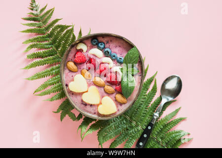 Gesundes Frühstück Banane und blueberry Smoothie mit Früchten in Coconut Schüssel auf rosa Hintergrund eingerichtet. Blick von oben. Sauber Essen, vegetarische fo Stockfoto