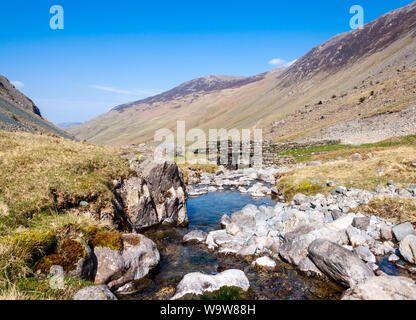 Die Gatesgarthdale Beck Gebirgsbach fließt unter einer Brücke aus Stein auf der Honister Pass Road hoch in den Bergen des englischen Lake District. Stockfoto