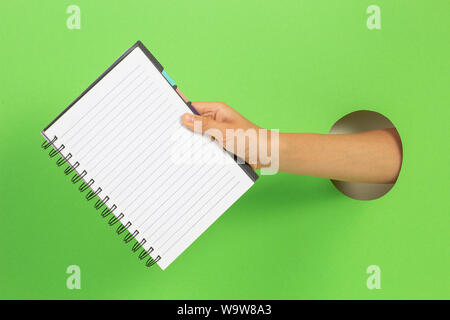 Kid Holding offene Spirale Notebook in der Hand durch die Öffnung auf der hellgrünen Hintergrund Stockfoto