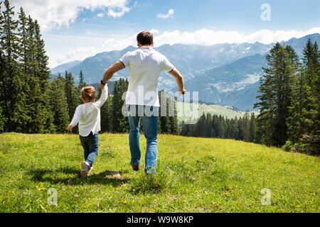 Vater und Tochter halten sich an den Händen, die auf Feld, in den Bergen Stockfoto