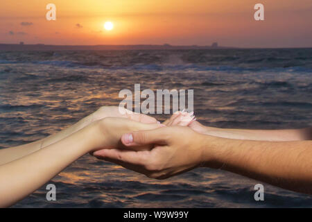 Sie verfingen sich die Sonne in ihre Familien. Sunrise. Hände im Hintergrund der Sonne und des Himmels. Hände halten einander auf See und Sonne. Zwei Stockfoto