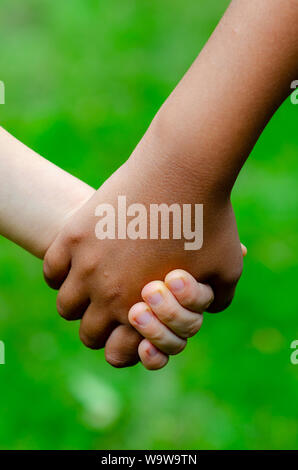 Junge und Mädchen verschiedener Rassen halten Hände zusammen. Junge ist Kaukasisch (weiß) und das Mädchen ist Schwarz. Konzept für Freundschaft, Frieden, Support, Gleichstellung von Frauen und Männern. Stockfoto